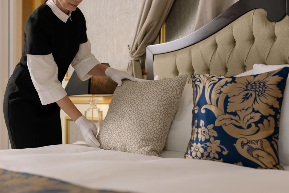 Hotel housekeeper arranging cushions on a freshly made bed in a hotel room